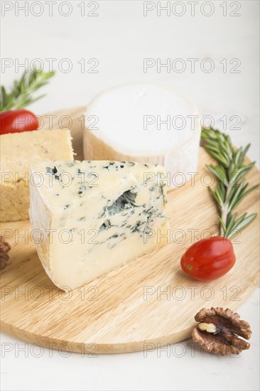 Blue cheese and various types of cheese with rosemary and tomatoes on wooden board on a white