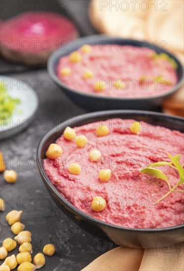 Hummus with beet and microgreen basil sprouts in ceramic bowl on a black concrete background and