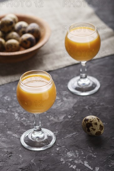 Sweet egg liqueur in glass with quail eggs on a black concrete background. Side view, low key,