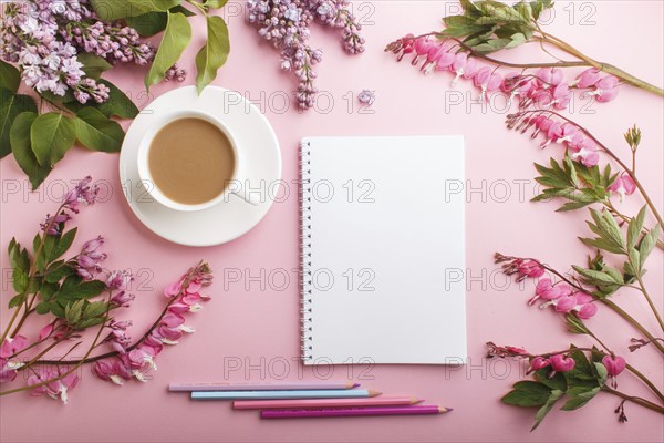 Purple lilac and bleeding heart flowers and a cup of coffee with notebook and colored pencils on