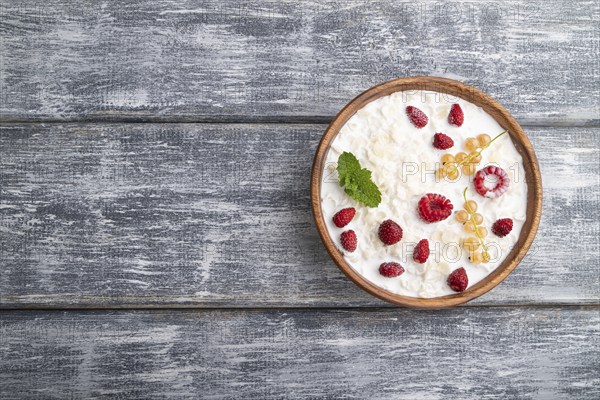 Rice flakes porridge with milk and strawberry in wooden bowl on gray wooden background. Top view,