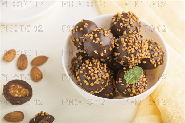 Chocolate caramel ball candies with almonds and a cup of coffee on a white wooden background and