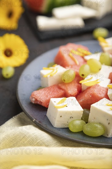 Vegetarian salad with watermelon, feta cheese, and grapes on blue ceramic plate on black concrete