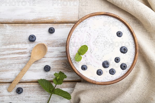 Yogurt with blueberry in wooden bowl on white wooden background and linen textile. top view, flat