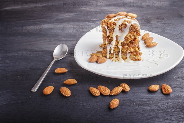 Pie with caramel, white milk sauce and almonds on a white plate on a black wooden background. close