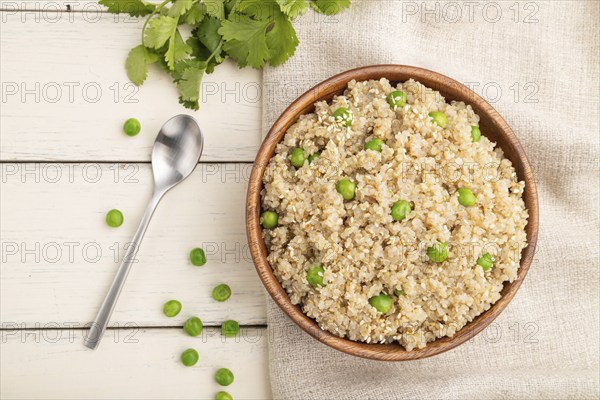 Quinoa porridge with green pea in wooden bowl on a white wooden background and linen textile. Top
