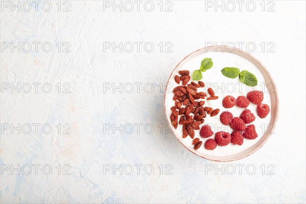 Yogurt with raspberry and goji berries in ceramic bowl on white concrete background. top view, flat