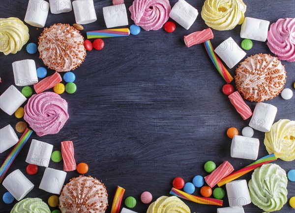 Colorful frame of multicolored candies on black wooden background. Circle copy space, top view,
