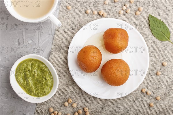 Traditional indian candy gulab jamun in white plate with mint chutney on a gray concrete background
