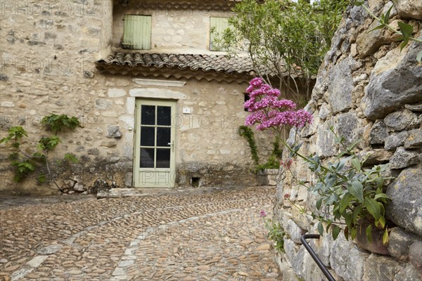 Natural stone wall with a red spur flower (Centranthus ruber) and old house with a door and roof in