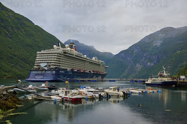 A large cruise ship, my ship 6, lies in the harbour of a fjord, surrounded by smaller boats and