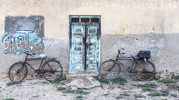 Old bicycles leaning against a house wall with an old wooden door, on the beach of Salalah, Dhofar