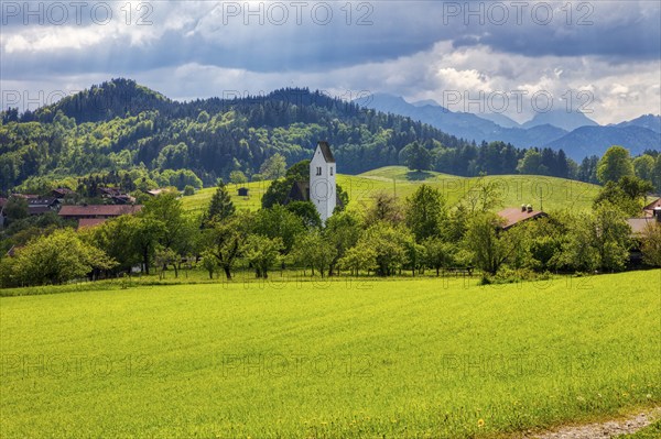 Rural scenery with church, green fields and hills under a cloudy sky, Steinkirchen