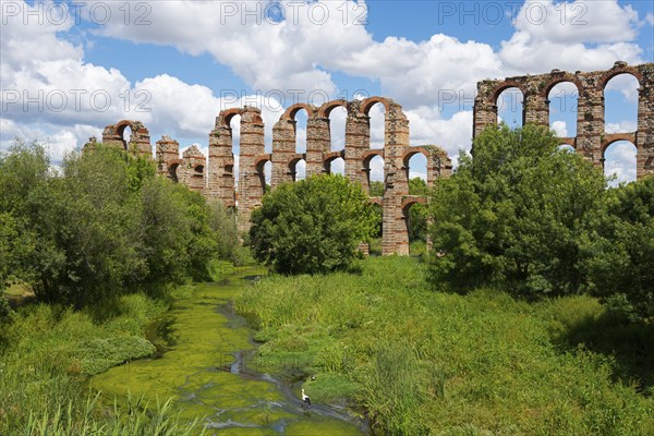 Antike Aquädukt-Ruinen inmitten von üppiger Vegetation und Fluss unter blauem Himmel, Acueducto de