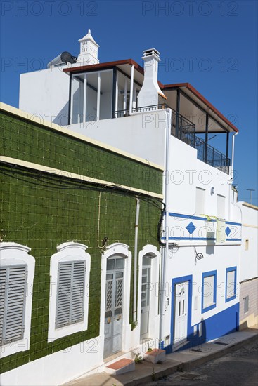Modern house with green tiles and white facade. Balconies and windows, blue sky in the background,