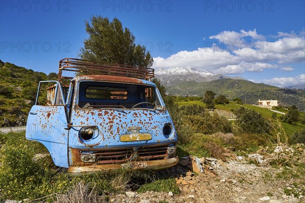 Abandoned rusty blue car on a green field with mountains in the background, wrecked vehicle, Crete,