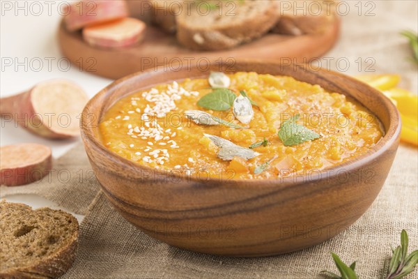Sweet potato or batata cream soup with sesame seeds in a wooden bowl on a white wooden background