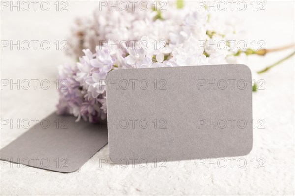 Gray business card with lilac flowers on gray concrete background. side view, copy space, mockup,