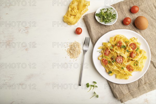 Reginelle semolina pasta with tomato, eggs, sesame and microgreen sprouts on a white wooden