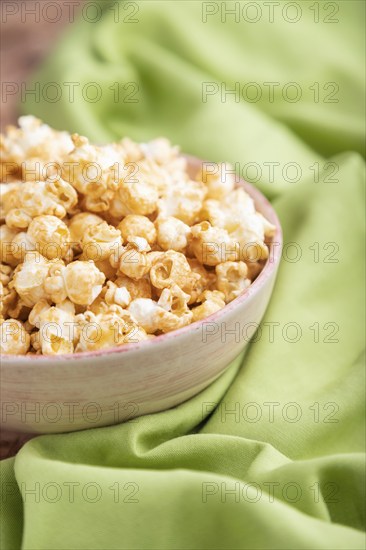 Popcorn with caramel in ceramic bowl on brown concrete background and green textile. Side view,