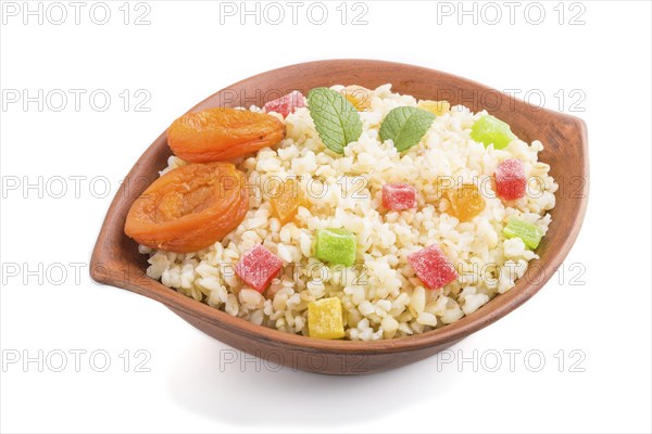 Bulgur porridge with dried apricots and candied fruits in clay bowl isolated on white background.