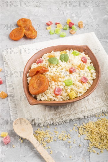 Bulgur porridge with dried apricots and candied fruits in clay bowl on a gray concrete background