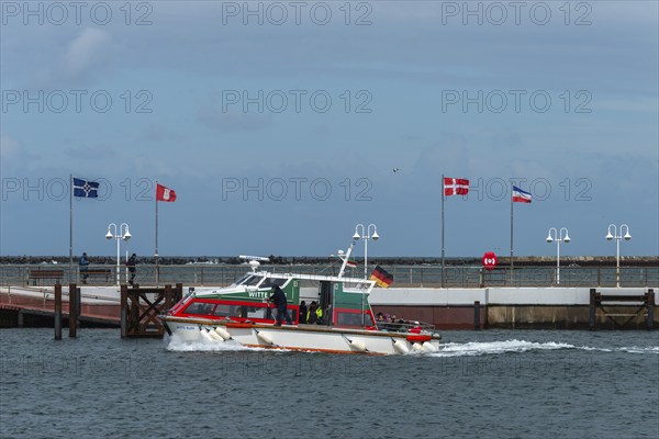 Dune ferry arrives in Heligoland harbour, flags in the wind, pier, offshore island of Heligoland,