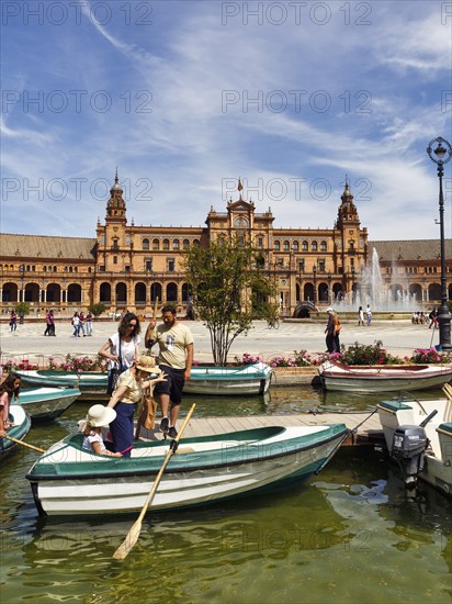 Tourists in rowing boats on a canal, pedestrians on Plaza de Espana, Plaza de España, Seville,