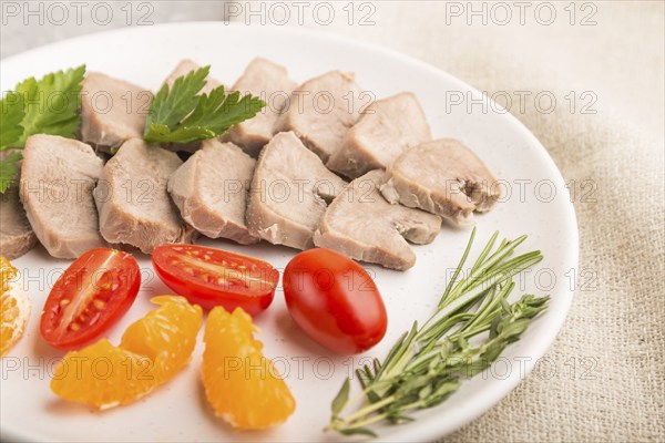 Boiled pork tongue with tomatoes and herbs on a gray concrete background and linen textile. Side