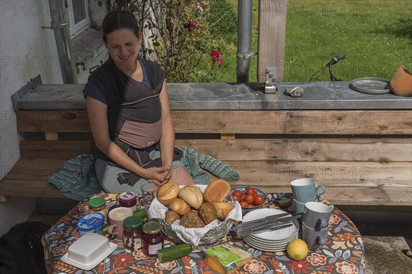 Young mum with baby in a sling at the breakfast table on the terrace, Mecklenburg-Vorpommern,
