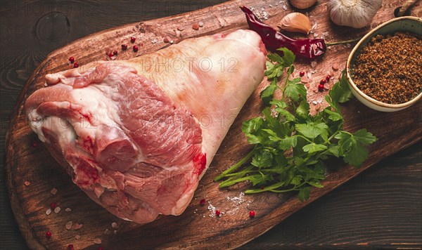 Raw pork knuckle, on a wooden chopping board, with spices, close-up, top view, no people