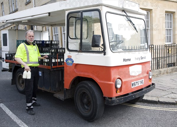 Milkman and traditional milk float home delivery service vehicle, Bath, Somerset, England, UK