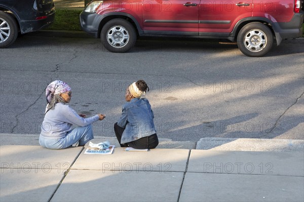 Detroit, Michigan, Two women sit on the curb outside the Shepherd art gallery during its grand