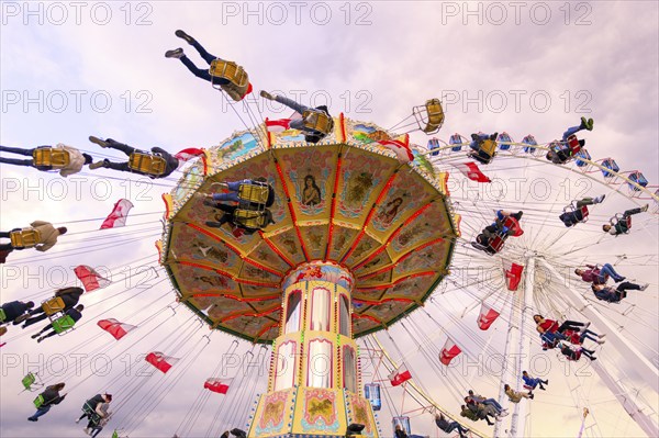 Chain carousel in motion with cheerful people in front of a cloudy sky, Ferris wheel, wave flight,