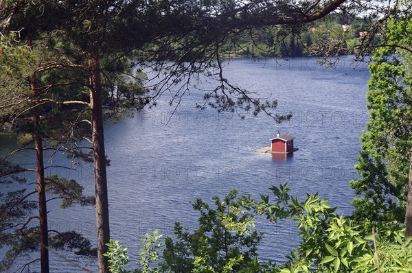 A tranquil scene by a lake with a red cabin in the water surrounded by dense green trees in the