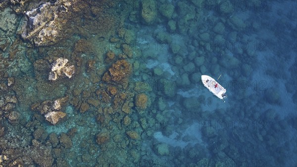 Drone shot, boat in crystal clear blue water between rocks and corals, Anthony Quinn Bay, Vagies