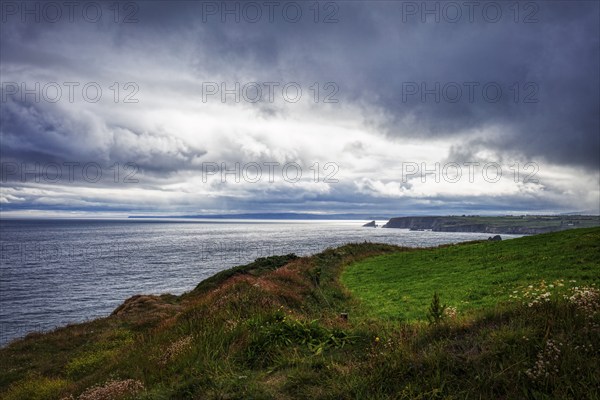 Dramatic coastal landscape with cloudy skies and green meadows bordering the cliffs, Waterford