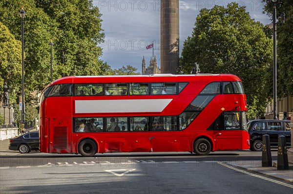 A red double-decker bus with a free advertising space or banner drives through a tree-lined street