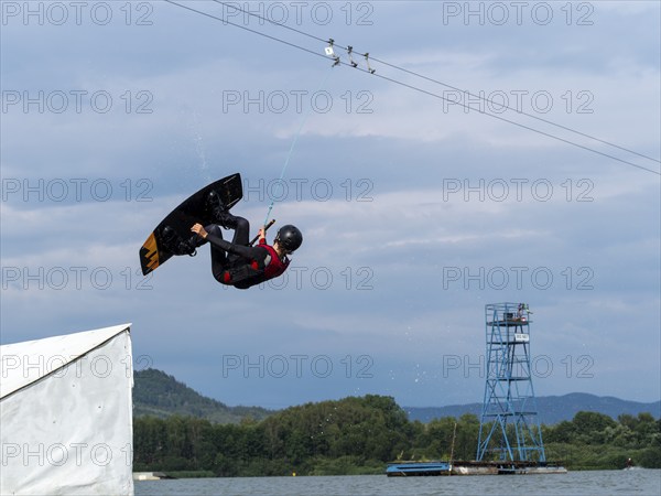 Man jumping with wakeboard over obstacle, somersault, water sports, water skiing and wakepark,