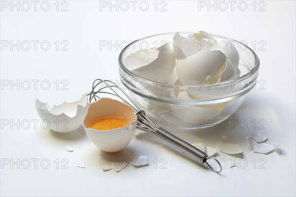Egg shells in a glass bowl, whisk and opened hen's egg