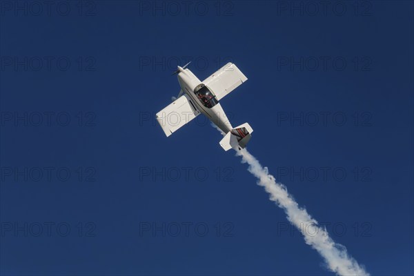 Stunt aerobatic plane performing stunts in blue sky with smoke trail. Concept of speed, difficulty,