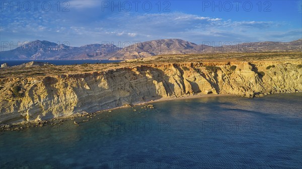 Coastal landscape with calm water and rocky cliffs under blue sky, drone shot, evening light,