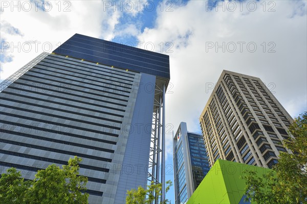 Modern skyscrapers with a backdrop of a blue sky and scattered clouds, surrounded by trees and