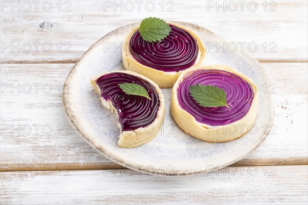 Sweet tartlets with jelly and milk cream on a white wooden background. Side view, close up