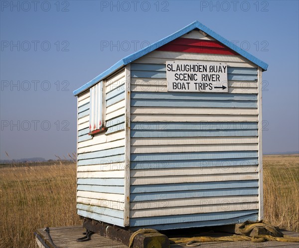 Old seaside beach hut with notice sign for boat trips at Slaughden, Aldeburgh, Suffolk, England,