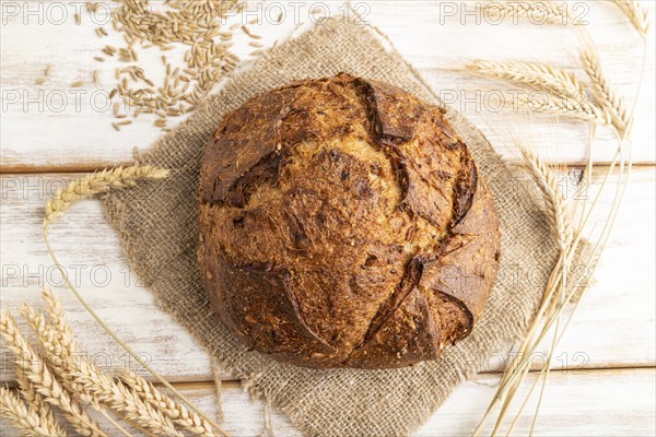 Fresh homemade golden grain bread with ears of wheat and rye on white wooden background and linen