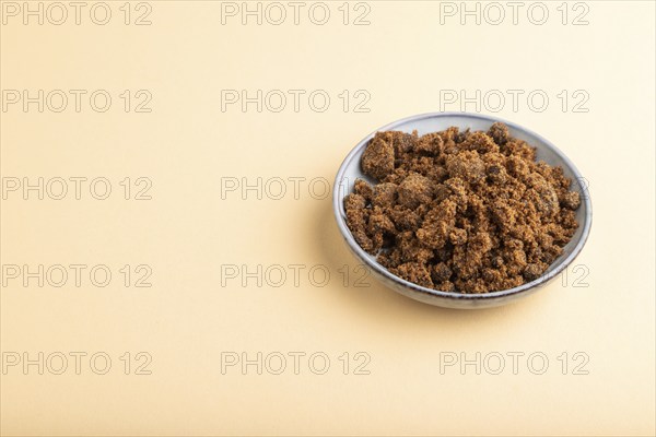 Plate with unrefined brown cane sugar on orange pastel background. side view, copy space
