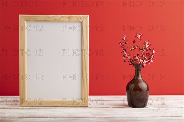 Wooden frame with purple barrenwort flowers in ceramic vase on red pastel background. side view,
