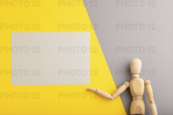 Wooden mannequin holding gray blank poster on gray and yellow pastel background. copy space,