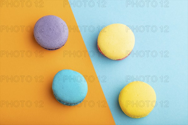 Yellow, purple and blue macaroons on blue and orange pastel background. top view, copy space, close